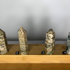 May include: Four green, brown, and white striped crystal points on a wooden display stand. The points are numbered 1 through 4.
