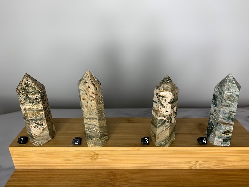 May include: Four green, brown, and white striped crystal points on a wooden display stand. The points are numbered 1 through 4.