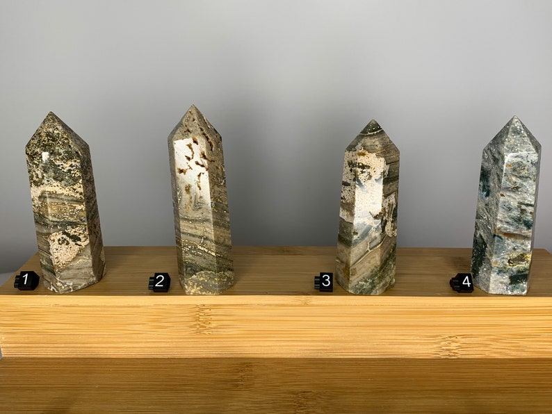 May include: Four green, brown, and white striped crystal points on a wooden display stand. The points are numbered 1 through 4.