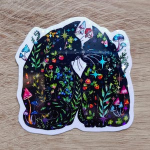 Può includere: Un adesivo con due gatti neri che si fronteggiano, riempiti di illustrazioni colorate di funghi, bacche e fogliame. L'adesivo ha una finitura olografica e un bordo bianco.