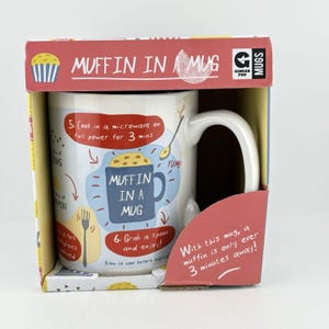 May include: A white ceramic mug packaged in a red and yellow cardboard box. The mug features printed instructions and illustrations for making a muffin, including the text Muffin in a Mug, 5. Cook in a microwave on full power for 3 mins, and 6. Grab a spoon and enjoy!