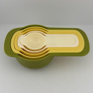 Può includere: Un set nidificato di misurini nei toni del verde, giallo e crema. Il set include un contenitore esterno verde, con il marchio "Joseph Joseph" stampato sul lato dei cucchiai dosatori.