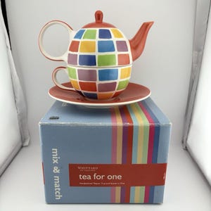May include: A tea for one set featuring a teapot, cup, and saucer stacked together. The pieces have a colourful grid pattern of red, blue, green, and yellow squares. The set sits on a blue box labelled Whittard of Chelsea mix & match tea for one.