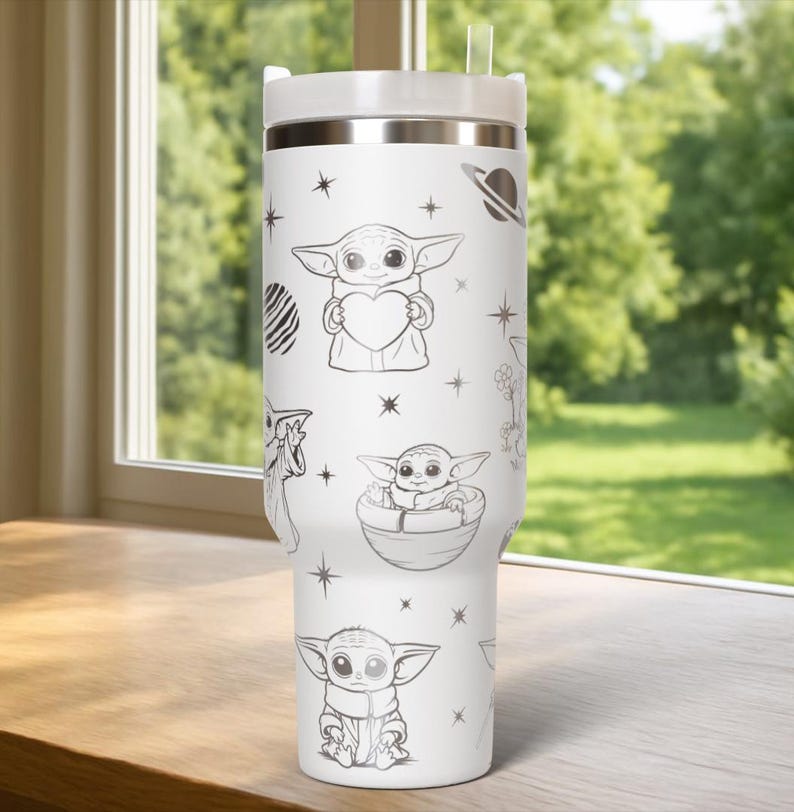 May include: White stainless steel tumbler with a silver lid and straw. The tumbler is decorated with black and white illustrations of a character holding a heart, in a pod, and other space-themed designs. The tumbler is sitting on a wooden surface.