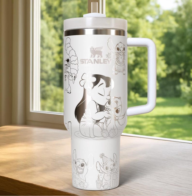 May include: White Stanley tumbler with a handle, featuring a design of Lilo & Stitch characters. The tumbler has a white lid and handle, with the Stanley logo. The design includes illustrations of Lilo, Stitch, and other characters from the movie.