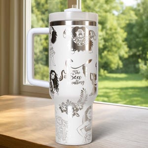 May include: White insulated tumbler with a handle, featuring silver illustrations of characters and floral designs. The text "The Sea is Calling" is also displayed. The tumbler has a white lid and handle.