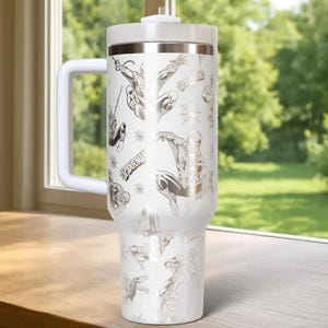 Puede incluir: Vaso t&eacute;rmico blanco con asa, con un patr&oacute;n repetido de ilustraciones de Spider-Man en plata. El vaso tiene una tapa blanca y una banda plateada en la parte superior. Tambi&eacute;n se ve la palabra "SPIDER-MAN".