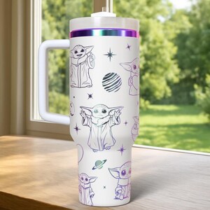 May include: White travel mug featuring illustrations of a character in a robe, with a handle and a lid. The mug has a purple and iridescent band around the top. The design includes stars and planets.