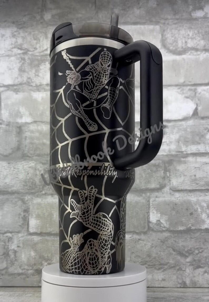 Puede incluir: Vaso de acero inoxidable negro con un dise&ntilde;o plateado de Spider-Man. El vaso tiene un asa, una tapa y una pajita. El dise&ntilde;o incluye a Spider-Man y el texto "With Great Responsibility".