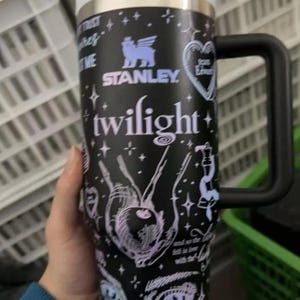 May include: Black Stanley tumbler with a white lid and handle, featuring "Twilight" text and related graphics. The design includes stars, eyes, and the words "Breaking Dawn." The tumbler has a capacity of approximately 30 ounces.