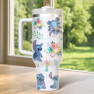 Peut inclure: Gobelet blanc avec Stitch de Lilo & Stitch, avec des motifs floraux. Le gobelet a une poign&eacute;e et un couvercle blancs. Le motif comprend Stitch dans diverses poses, entour&eacute; de fleurs color&eacute;es et de feuilles vertes. Le gobelet est con&ccedil;u pour contenir une grande quantit&eacute; de liquide.