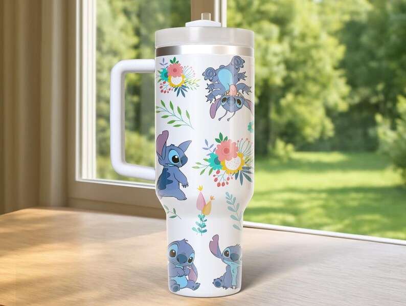 Peut inclure: Gobelet blanc avec Stitch de Lilo & Stitch, avec des motifs floraux. Le gobelet a une poign&eacute;e et un couvercle blancs. Le motif comprend Stitch dans diverses poses, entour&eacute; de fleurs color&eacute;es et de feuilles vertes. Le gobelet est con&ccedil;u pour contenir une grande quantit&eacute; de liquide.
