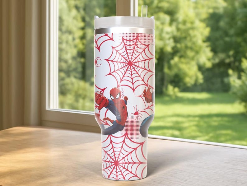 May include: A white tumbler featuring a red spiderweb design and illustrations of Spider-Man. The tumbler has a white lid and a clear straw. The design wraps around the entire tumbler, creating a cohesive look.