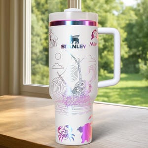 May include: White Stanley tumbler with a handle, featuring a colorful design with characters and imagery from a popular animated film. The tumbler has a white lid and a handle. The design includes the Stanley logo and the words "I'm so shiny".