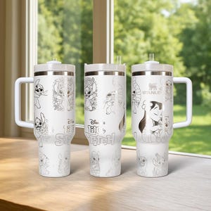 May include: Three white Stanley tumblers with silver-colored illustrations of Stitch from Disney's Lilo & Stitch. Each tumbler has a white handle, lid, and straw. The text "Disney Lilo & Stitch" is visible on the tumblers.