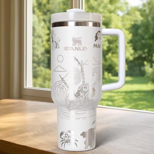 May include: White Stanley tumbler with a handle, lid, and straw. The tumbler features etched illustrations of characters and scenes from a popular animated movie. The Stanley logo is visible. The text "I'M SO SHINY" is also etched on the tumbler.