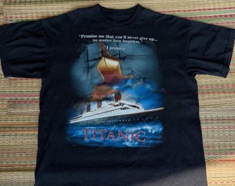 May include: Black t-shirt featuring a graphic from the movie Titanic. The design includes an image of the ship, a couple, and the text "TITANIC". The shirt also has the quote: "Promise me that you'll never give up... no matter how hopeless. I promise."