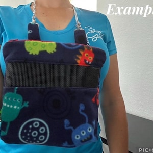May include: A navy blue fleece carrier with a black elastic band and a silver chain. The carrier is decorated with colorful cartoon monsters. The word "Example" is written in white on the top right.