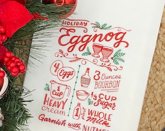 May include: White holiday kitchen towel with a red "Eggnog" recipe printed on it. The recipe includes ingredients like eggs, bourbon, heavy cream, sugar, and whole milk. The towel is decorated with festive illustrations and text.