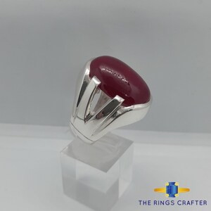 May include: A silver ring featuring a large, oval-shaped, dark red gemstone set in a contemporary design.