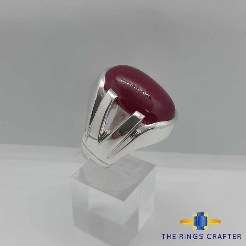 May include: A silver ring featuring a large, oval-shaped, dark red gemstone set in a contemporary design.