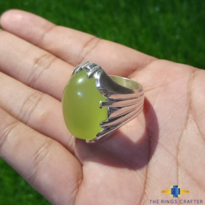 May include: A silver ring with a large, oval-shaped, light green gemstone. The ring has a detailed, ornate design.