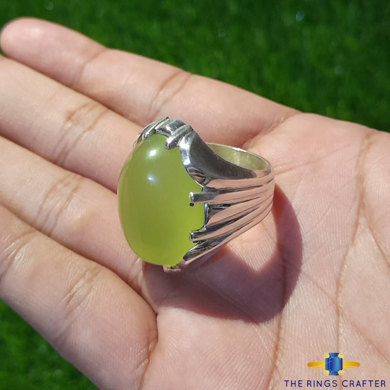 May include: A silver ring with a large, oval-shaped, light green gemstone. The ring has a detailed, ornate design.