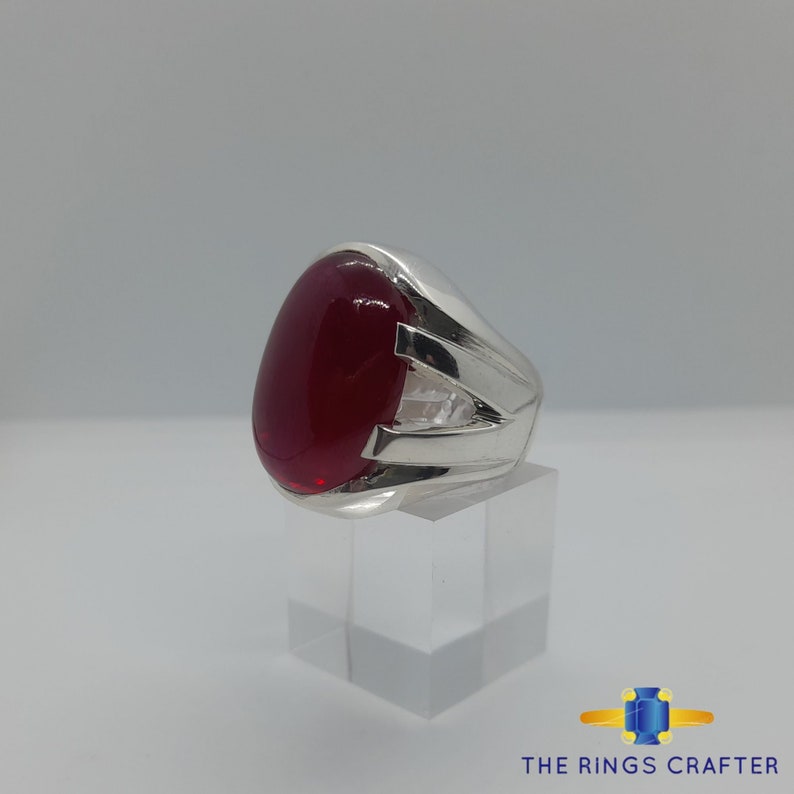 May include: A silver ring featuring a large, oval-shaped, red gemstone set in the centre. The ring has a simple, elegant design with three silver bands extending from the setting.