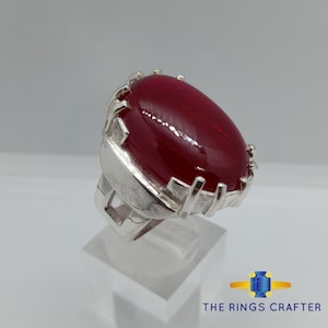 May include: A silver ring with a large, oval-shaped, red gemstone set in a detailed, silver setting.