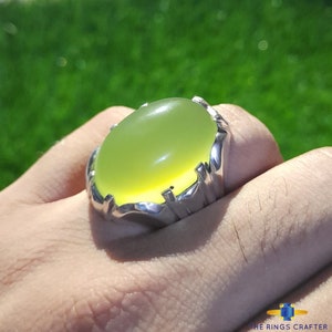 May include: A silver ring with a large, oval-shaped, light green gemstone. The ring is set in a silver band with a decorative design.