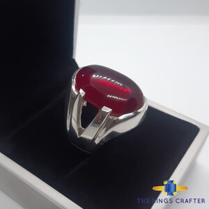 May include: A silver ring featuring a large, oval-shaped, red gemstone set in a V-shaped band.