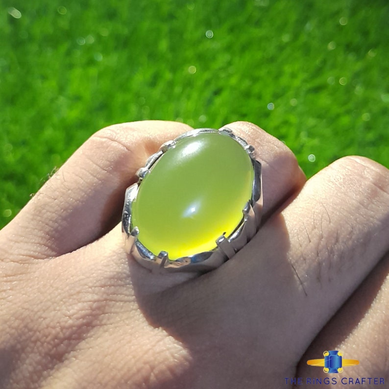 May include: A silver ring with a large, oval-shaped, light green gemstone. The ring has a detailed, ornate design.