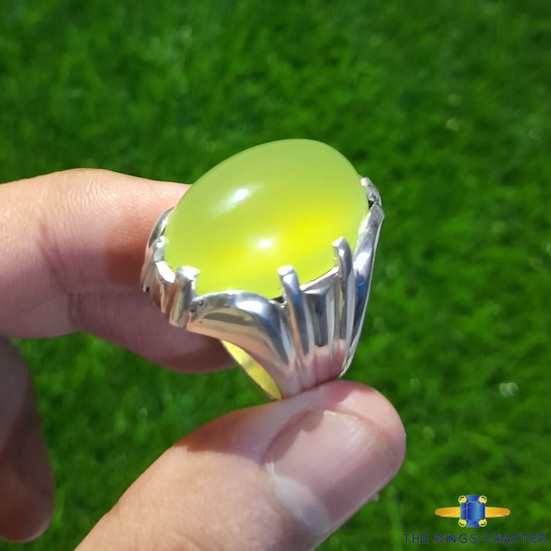 May include: A silver ring with a large, oval-shaped, bright green gemstone. The ring has a detailed, ornate design.
