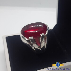 May include: A silver ring featuring a large, oval-shaped, deep red gemstone. The ring has a V-shaped design on the band.