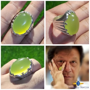 May include: A silver ring with a large, oval-shaped, light green gemstone. The ring has a detailed, ornate design.