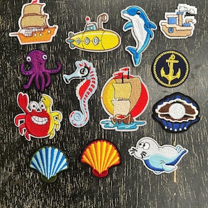 May include: A collection of colorful embroidered patches featuring nautical and marine life themes. Designs include a sailboat, submarine, dolphin, octopus, seahorse, crab, anchor, seashell, and a seal. These patches are perfect for adding to clothing or accessories.