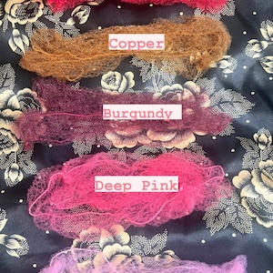 Puede incluir: Cinco redes para el cabello en diferentes colores: rojo, cobre, burdeos, rosa intenso y rosa pastel. Las redes para el cabello están dispuestas verticalmente sobre un fondo negro con un patrón floral.