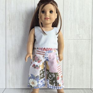 May include: A doll with long brown hair wearing a sleeveless top with thin white and light blue vertical stripes and wide-leg trousers featuring a patchwork design of various floral, striped, and gingham patterns in shades of blue, pink, and green.