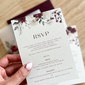 May include: A wedding RSVP card featuring a floral design in white and burgundy. The card displays the word "RSVP" and instructions for replying, plus menu choices: beef, chicken, pork, or veggie, and dessert options.