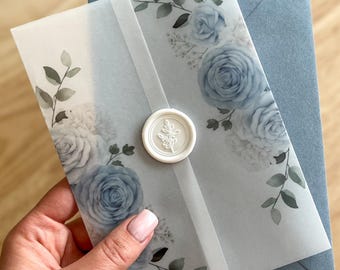 Puede incluir: Un sobre blanco con un diseño floral azul y un sello de cera blanco. El sobre es translúcido y tiene un patrón floral azul. El sello de cera es redondo y tiene un diseño de hoja.