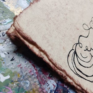 May include: A stack of thick, textured, light tan paper sheets with rough, deckled edges stained in a dark brown hue. A black ink line drawing featuring curved, abstract shapes is visible on the top sheet of the paper stack.