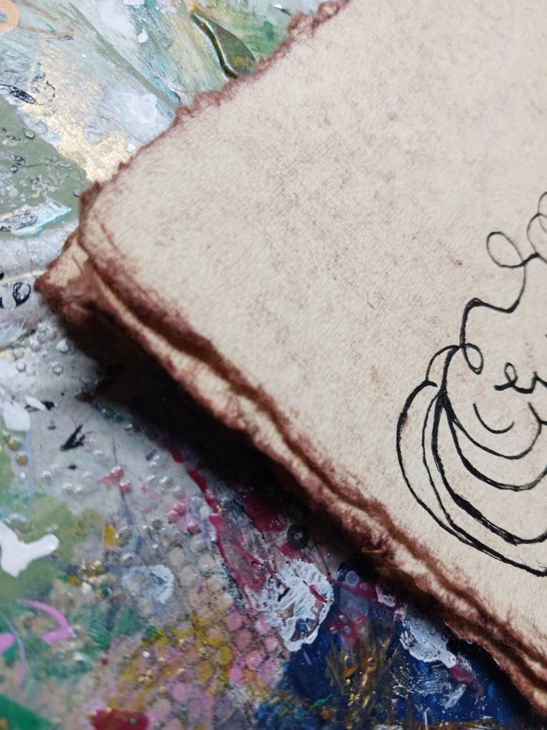 May include: A stack of thick, textured, light tan paper sheets with rough, deckled edges stained in a dark brown hue. A black ink line drawing featuring curved, abstract shapes is visible on the top sheet of the paper stack.