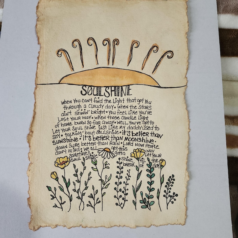 Pu&ograve; includere: Un'illustrazione disegnata a mano di un sole con le parole "SOULSHINE" scritte in inchiostro nero. Il testo sotto il sole dice: "Quando non riesci a trovare la luce che ti ha portato attraverso una giornata nuvolosa, quando le stelle non brillano, ti senti come se ti fossi perso. Quando quelle luci di candela a casa bruciano cos&igrave; lontano, beh, devi lasciare che la tua anima brilli come faceva mio padre. Parlando di anima, &egrave; meglio del sole, &egrave; meglio della luna. Certo che &egrave; meglio della pioggia. Signore, ora la gente non se ne preoccupa, dobbiamo tutti ottenere questa anima che brilla fino all'alba."