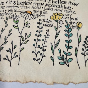 Pu&ograve; includere: Un'illustrazione disegnata a mano di fiori e piante su uno sfondo beige. I fiori sono gialli e bianchi, e le piante sono verdi e blu. Il testo "Shine a break of the day" &egrave; scritto in inchiostro nero.