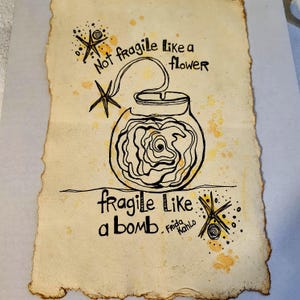 Puede incluir: Obra de arte dibujada a mano sobre papel envejecido. Un dibujo lineal negro representa una bomba con una rosa en su interior, conectada al texto "Not fragile like a flower" y "fragile like a bomb". La firma del artista, "Frida Kahlo", est&aacute; presente.