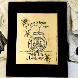 Puede incluir: Impresi&oacute;n art&iacute;stica enmarcada en negro con fondo amarillo y dibujo a tinta negra de una bomba con forma de flor. El texto dice: "Not fragile like a flower, fragile like a bomb - Frida Kahlo."