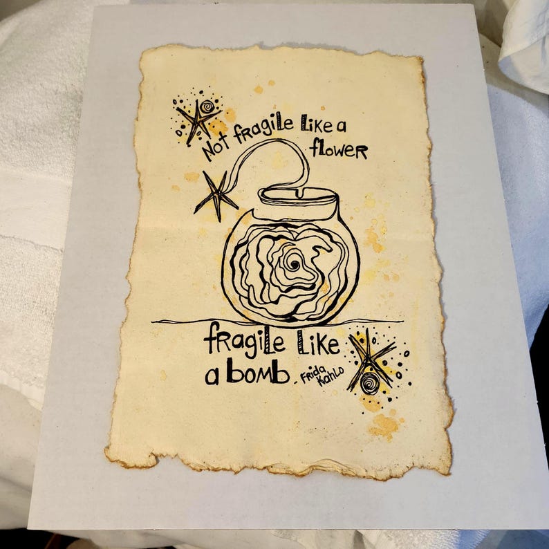 Puede incluir: Obra de arte dibujada a mano sobre papel envejecido. La imagen presenta un dibujo lineal negro de un tarro con una rosa en su interior, y el texto "Not fragile like a flower, fragile like a bomb. Frida Kahlo."