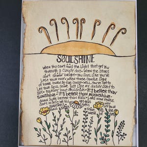 Pu&ograve; includere: Un'illustrazione disegnata a mano di un sole con raggi e le parole "SOULSHINE" in un font scritto a mano. Il testo sotto il sole recita: "Quando non riesci a trovare la luce che ti ha portato attraverso una giornata nuvolosa. Quando le stelle non brillano, ti senti come se ti fossi perso. Quando quelle luci di candela di casa bruciano cos&igrave; lontano. Beh, devi lasciare che la tua anima brilli come faceva mio padre. Parlando di SOULSHINE. &Egrave; meglio di SUNSHINE. &Egrave; meglio di MOONSHINE. Certo che &egrave; meglio della pioggia. Signore, ora la gente non se ne preoccupa. Abbiamo tutti questa strada. A volte, l'anima brilla. Brilla, devi rompere fino al giorno. Lascia che tu riempia il giorno."