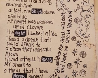 Puede incluir: Una hoja de papel color crema con letras de canciones escritas a mano en tinta negra. El texto incluye palabras resaltadas como Love, Skies, Night, Press y Never. Aparecen dibujos decorativos a tinta de nubes, estrellas y espirales.
