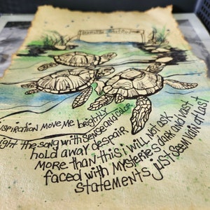 Op de afbeelding: Een stuk perkamentpapier met verbrande randen met een aquarel- en inktillustratie van drie zeeschildpadden die in blauw en groen water zwemmen. Het kunstwerk bevat handgeschreven tekst: Inspiration move me brightly, light the song with sense and color, hold away despair, more than this I will not ask, faced with mysteries dark and vast, statements just seem vain at last.